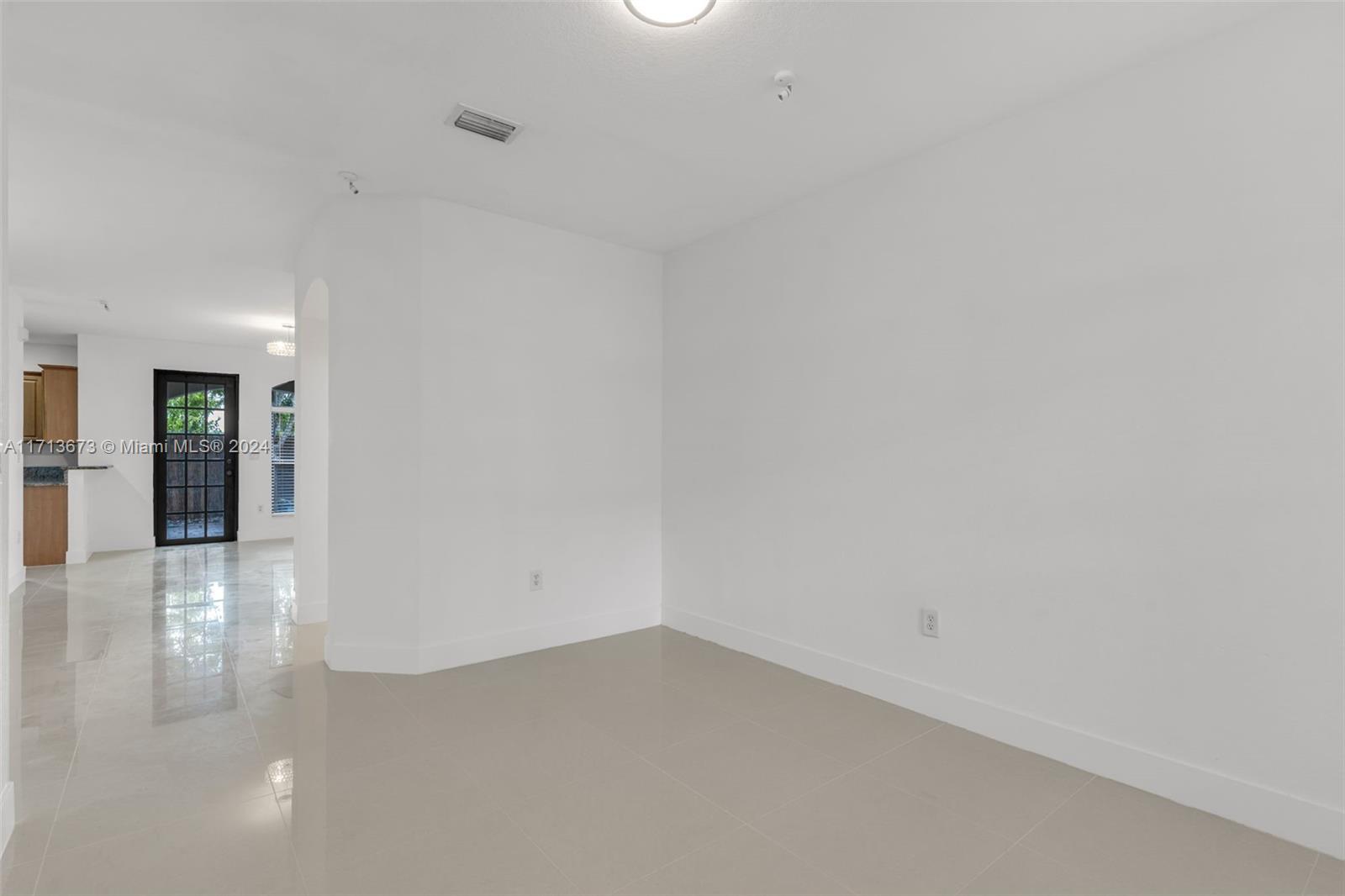 Empty tiled living area opening toward the kitchen and black-framed glass doors.