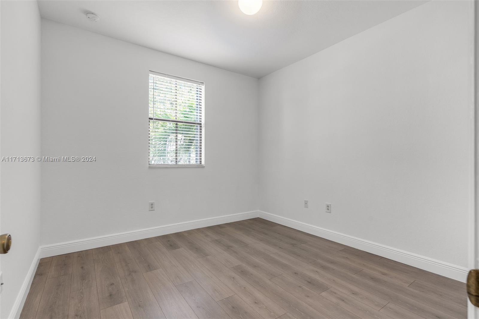 Empty room with wood-look flooring and a window with blinds.