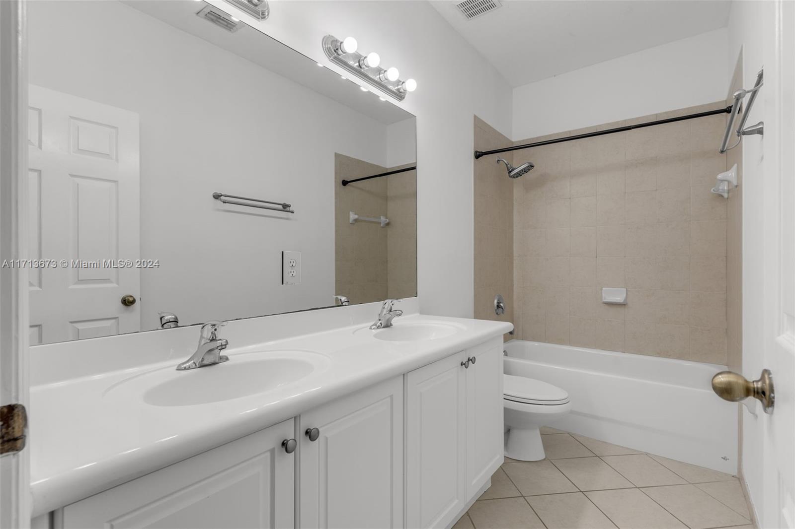 Bathroom with a double-sink vanity and a bathtub with beige tiled shower surround.