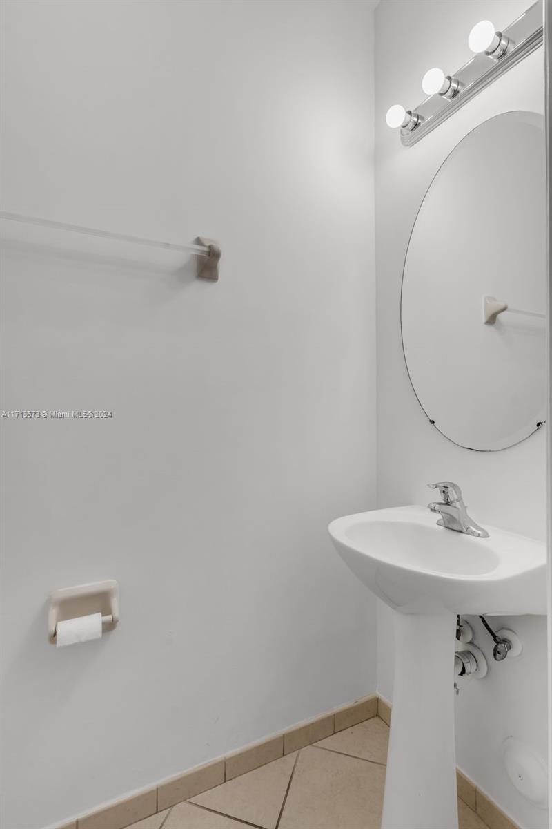 Bathroom with a white pedestal sink, large oval mirror, and three-bulb light fixture.