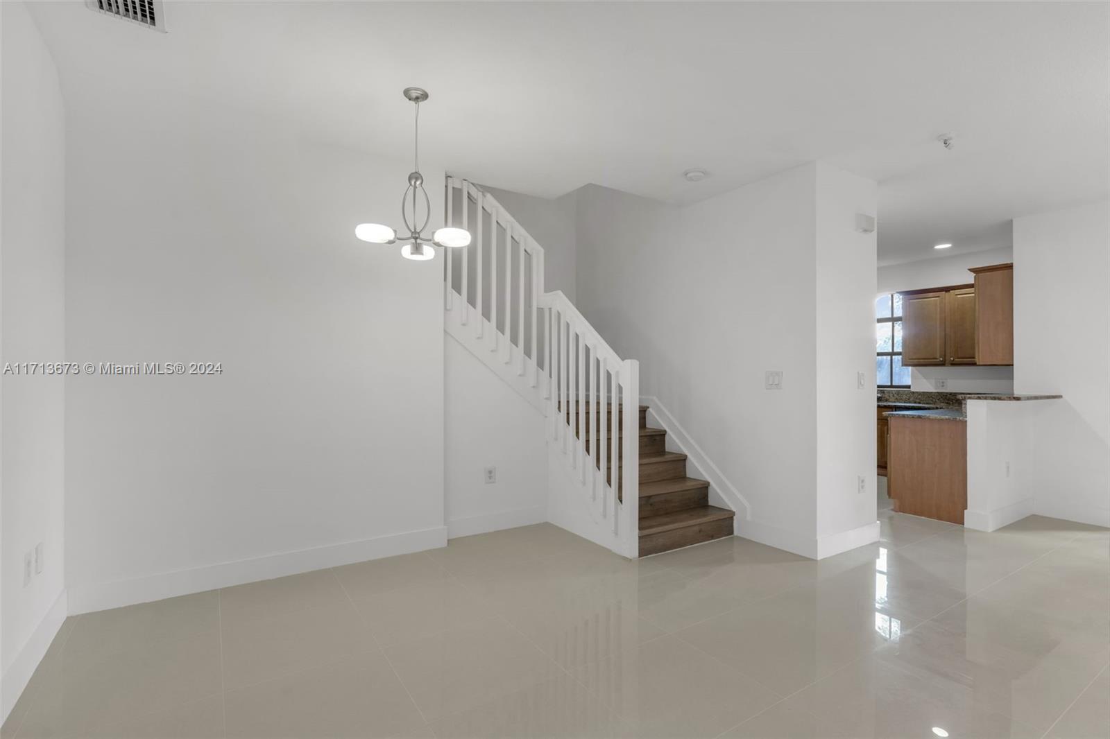 Bright tiled entry with a white-railed staircase and wood kitchen cabinets.