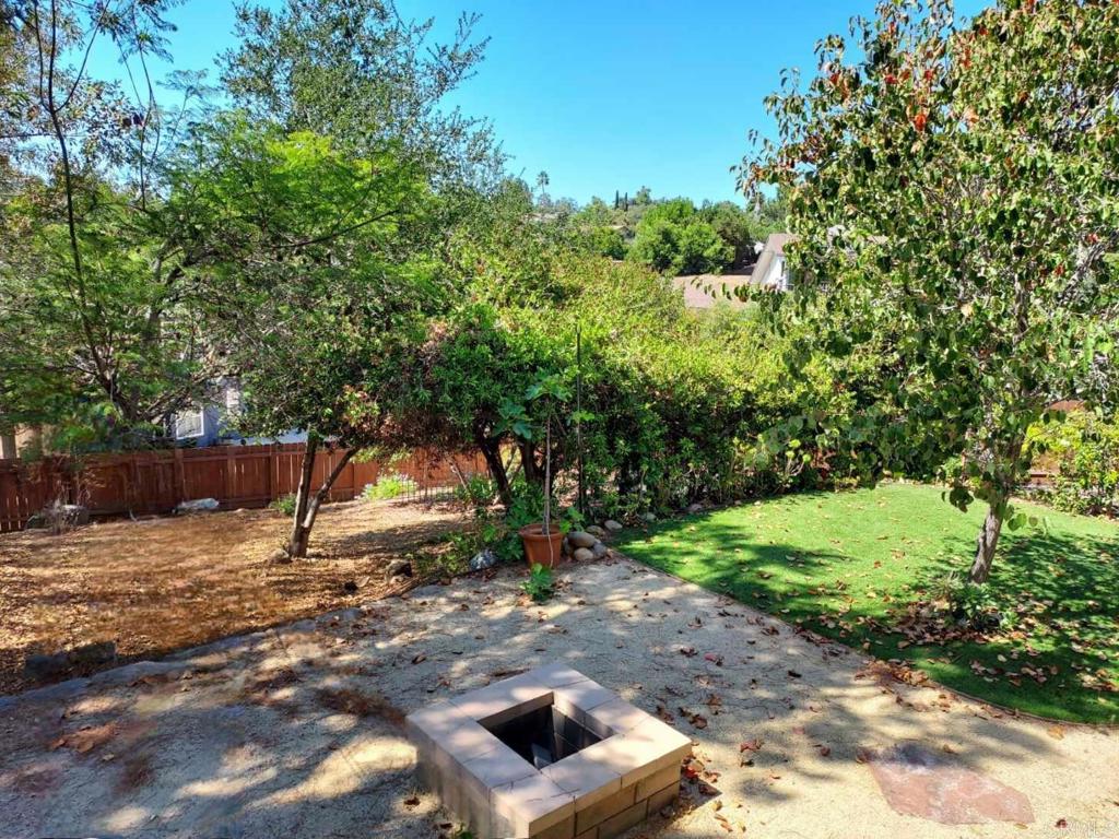 Backyard patio with a square fire pit, lawn, and mature trees.