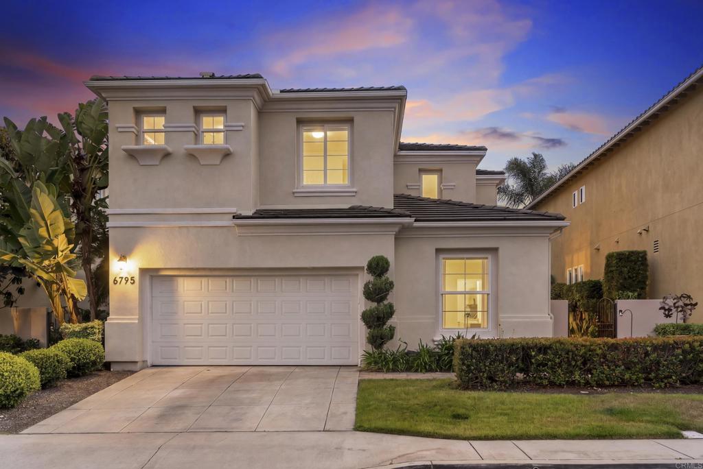 Two-story stucco home with a double garage, landscaped frontage, and glowing windows at dusk.