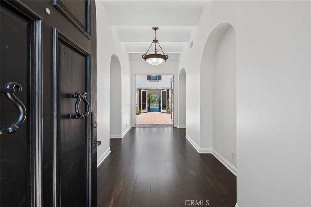Entry hallway with arched openings, dark flooring, and open doors to a tiled patio.