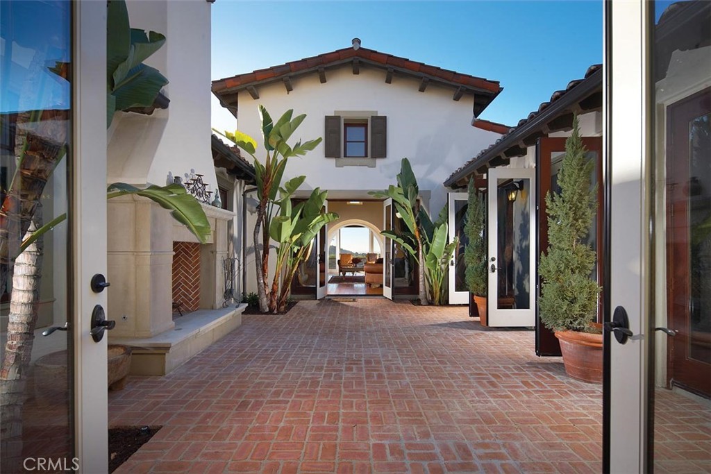 Brick-paved courtyard with tropical plants and open doors to a white stucco home.