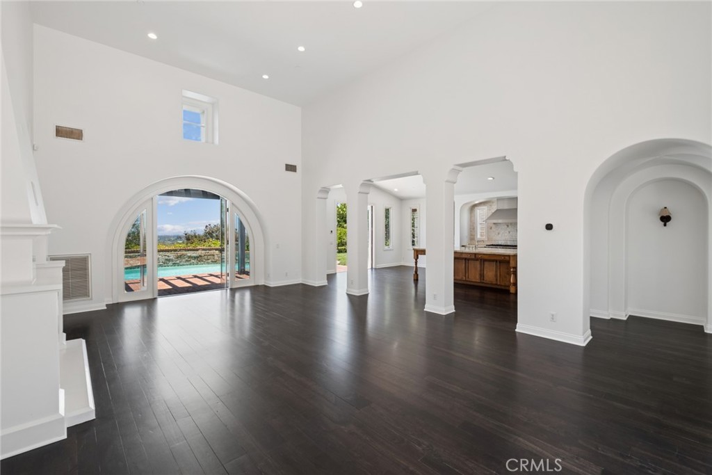 Vacant living room with dark wood floors, arched openings, and glass doors overlooking a pool.