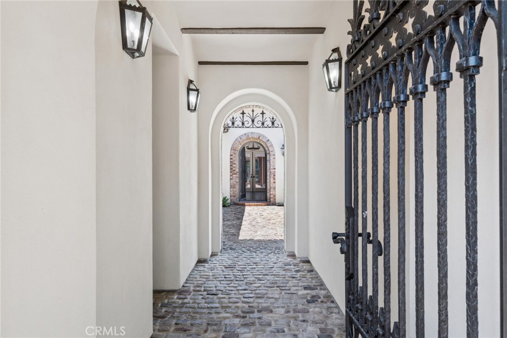 Arched entry passage with cobblestone flooring and an ornate black wrought-iron gate.