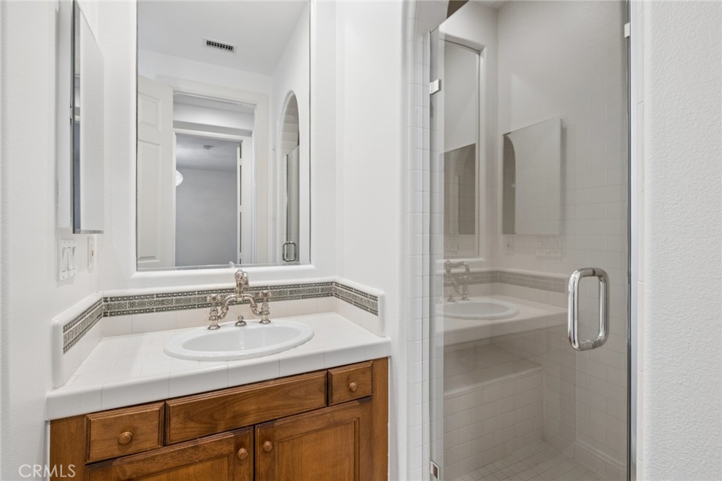 Bathroom with a wood vanity, oval sink, and glass-enclosed tiled shower.