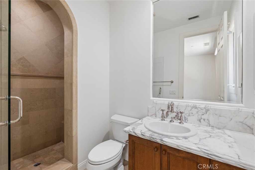 Bathroom with an arched tile shower, marble-patterned vanity top, and wood cabinetry.