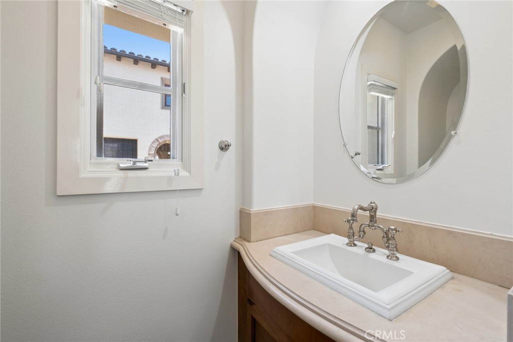 Bathroom vanity with a white sink, ornate chrome faucet, oval mirror, and window.