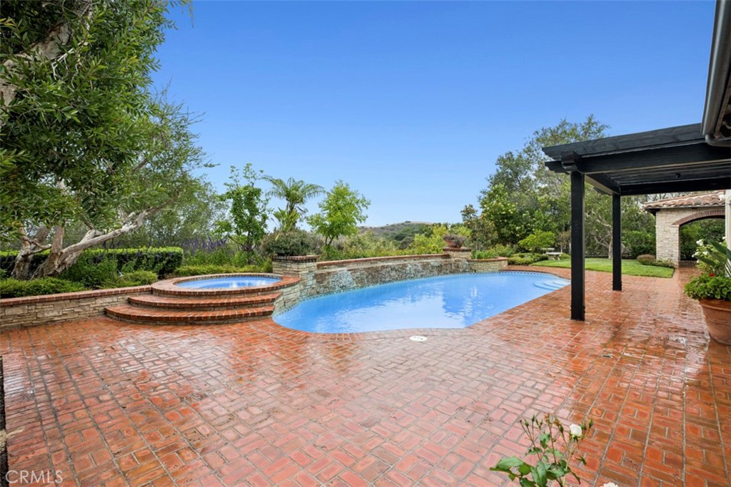 Backyard swimming pool and raised spa bordered by stone, with a wide brick patio.