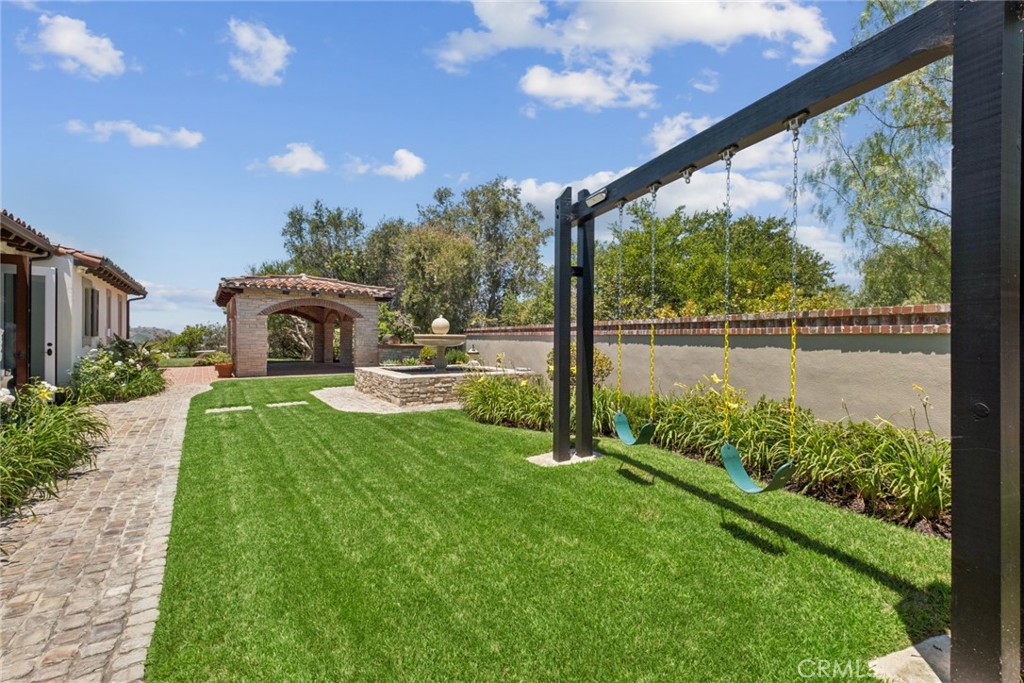 Backyard with a broad lawn, hanging swings, brick gazebo, stone fountain, and paved path.