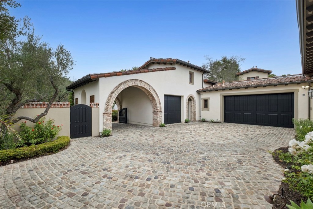 Spanish-style home with a stone-trimmed arched entry and broad cobblestone driveway.