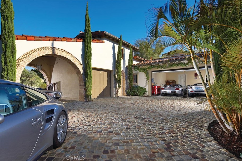 Mediterranean-style home with a brick archway, cobblestone driveway, palm trees, and garage.