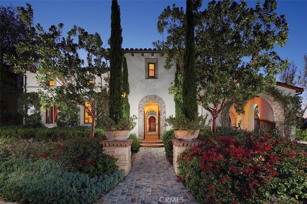 Mediterranean-style home at dusk with a stone-arched entrance and landscaped walkway.