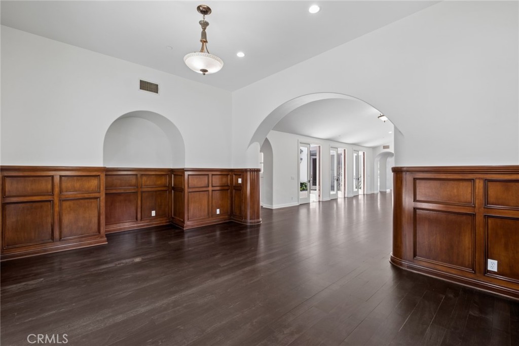 Empty room with dark wood floors, paneled wainscoting, and arched openings.