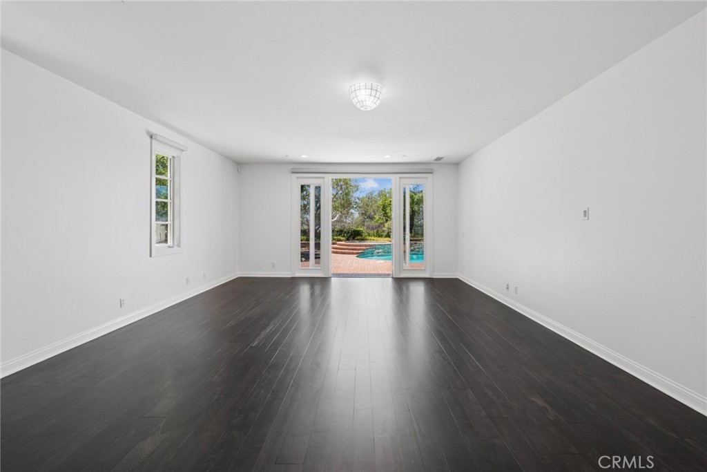 Vacant living room with dark wood floors and sliding doors opening to a poolside patio.