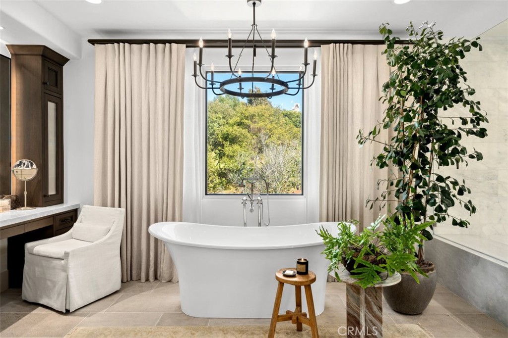 Staged bathroom with a freestanding tub, a window framed by cream curtains, and leafy potted plants.