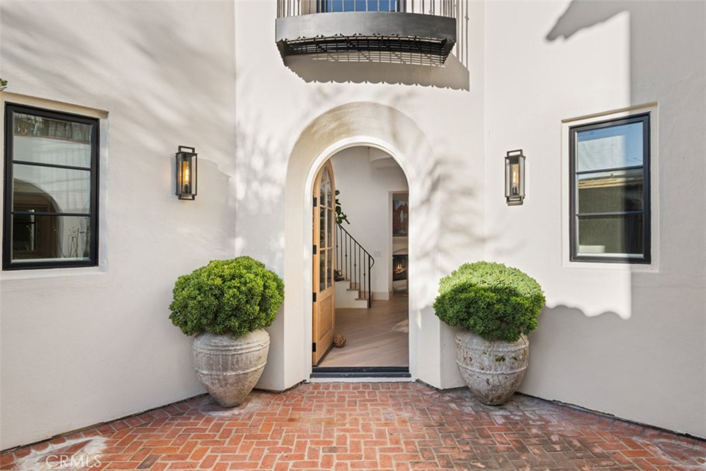 Home entrance with an arched doorway, brick paving, and matching potted shrubs.
