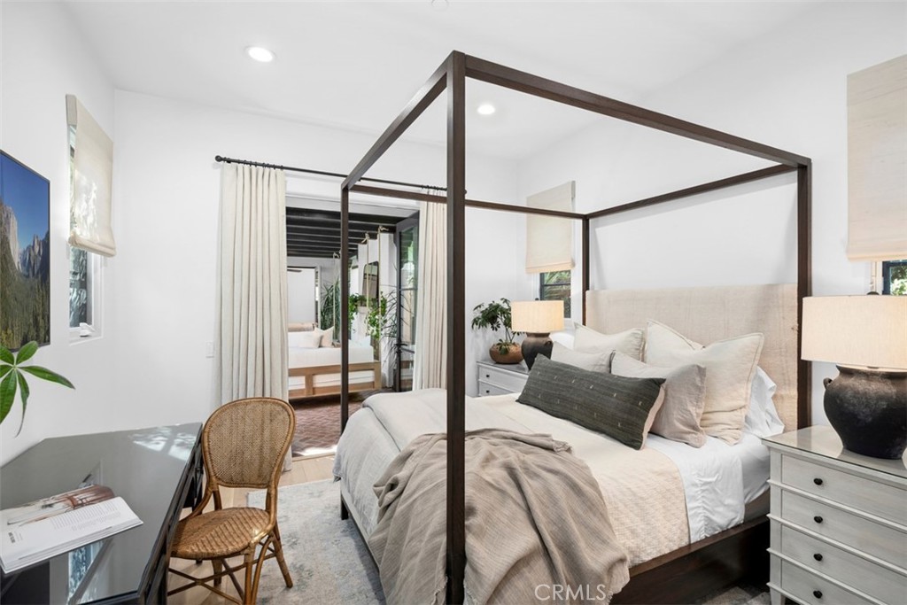 Bedroom with a dark wood canopy bed, neutral bedding, and a small desk with woven chair.