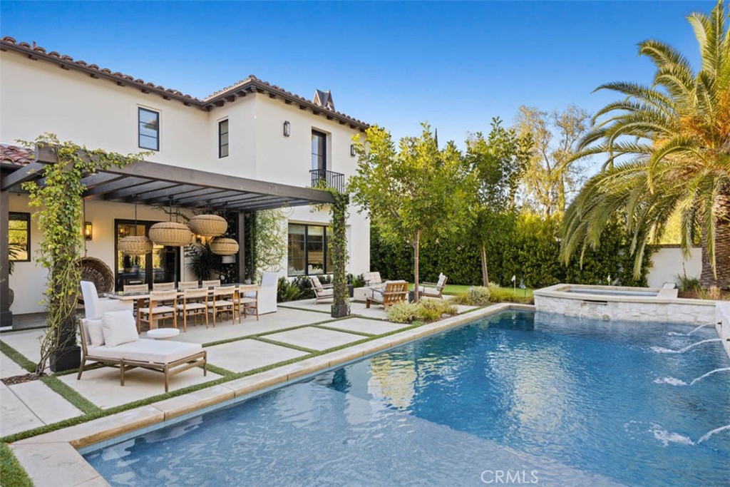 Two-story home beside a backyard pool, with a pergola-covered dining patio and palm trees.