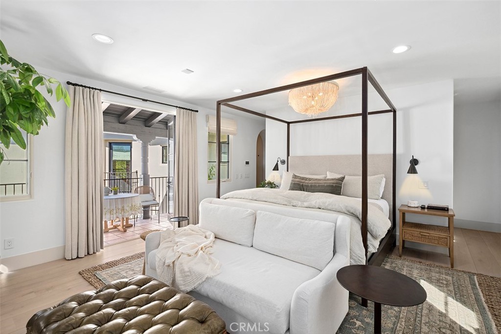 Bright bedroom with a dark four-poster bed, white sofa, chandelier, and doors opening to a patio.