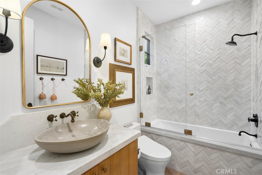 Bathroom with a marble vanity and vessel sink beside a glass-enclosed, herringbone-tile tub and shower.