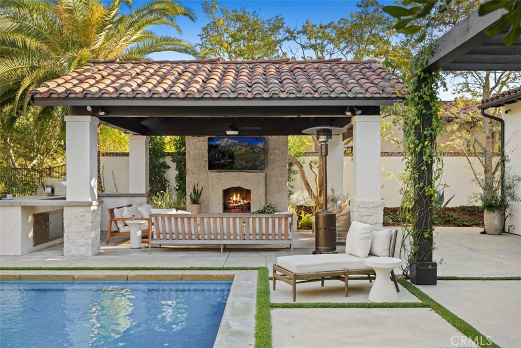 Backyard pool beside a furnished covered patio with a fireplace and outdoor kitchen.
