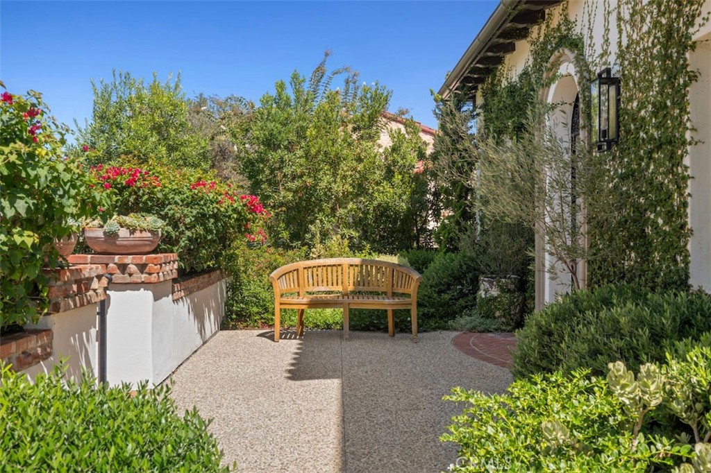 Landscaped courtyard with a wooden bench, brick-edged planters, and flowering vines beside the house.