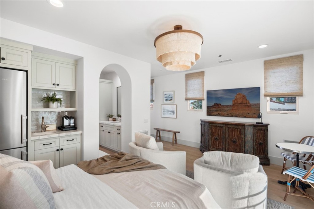 Living room with white seating, a compact kitchenette, arched bathroom entrance, and rustic sideboard.