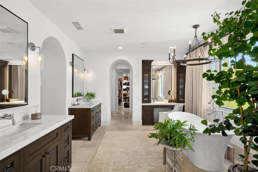 Primary bathroom with dark wood vanities, freestanding tub, arched doorway, and chandelier.