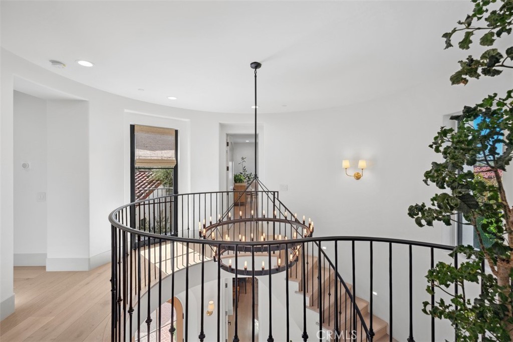 Upstairs landing overlooking an open staircase, with curved black railing and a large chandelier.