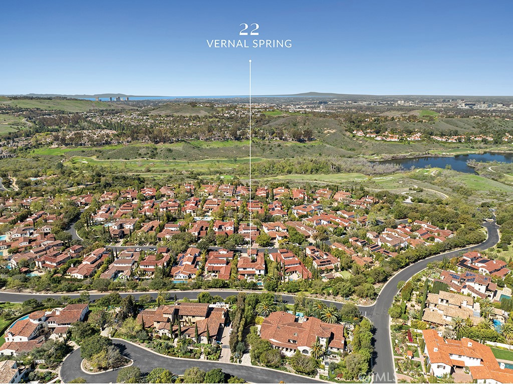 Aerial view of red-tile-roof homes beside green open space and a small body of water.