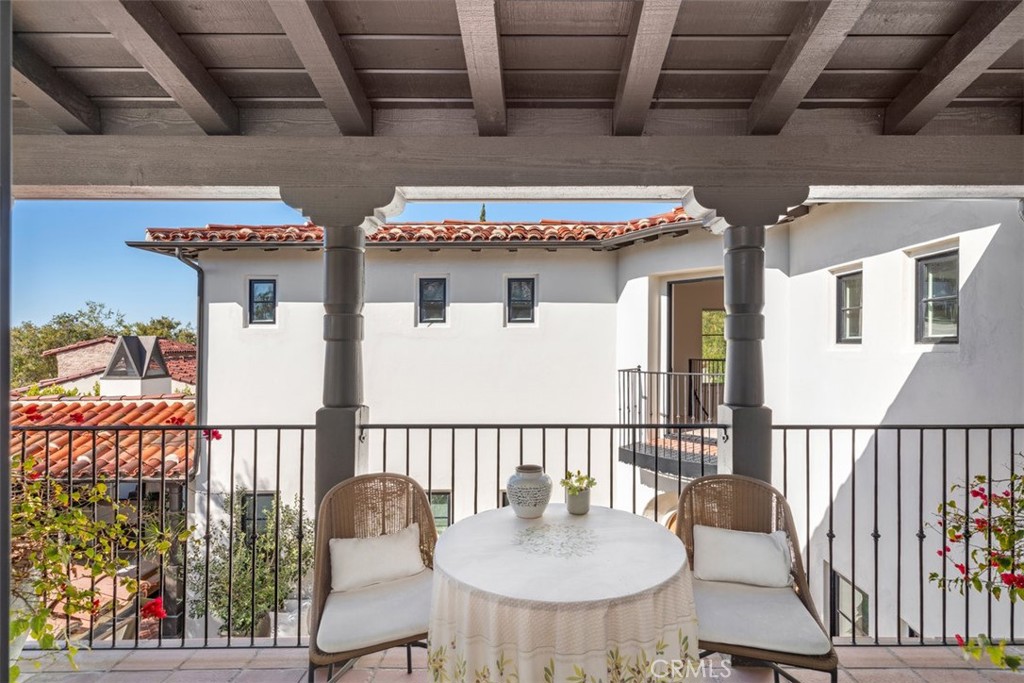 Covered balcony with a wood pergola, iron railing, and round table between two chairs.