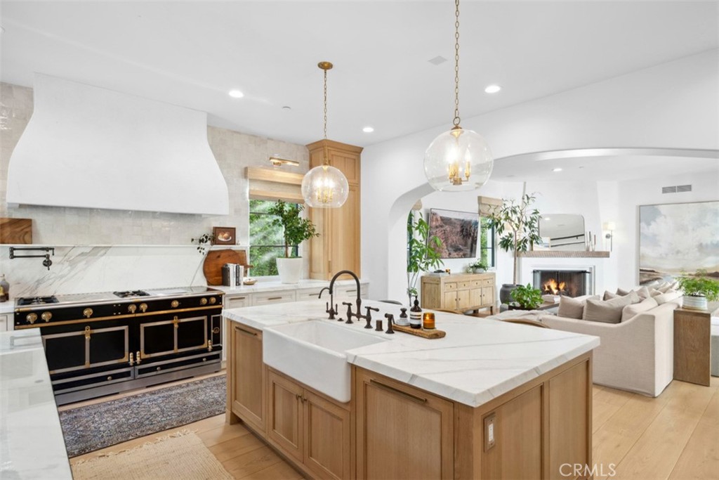 Kitchen with a large marble island, light wood cabinetry, and a black-and-brass range.