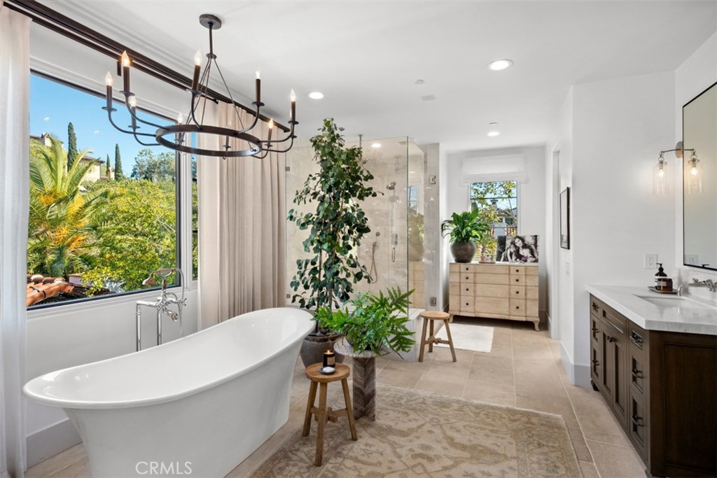 Spacious bathroom with a freestanding tub beside a large window and leafy greenery.