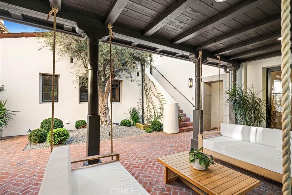 Covered brick courtyard patio with hanging rope swings, a tree, and white lounge seating.