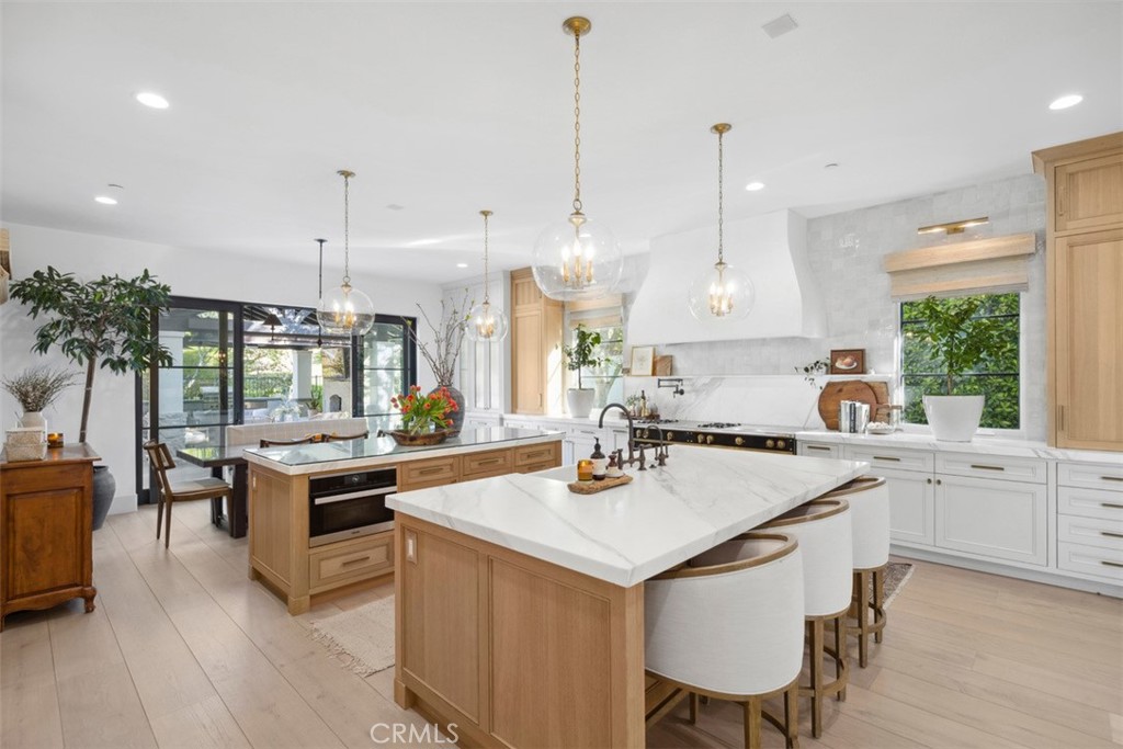 Bright kitchen with two marble islands, light wood cabinetry, and black-framed glass doors.