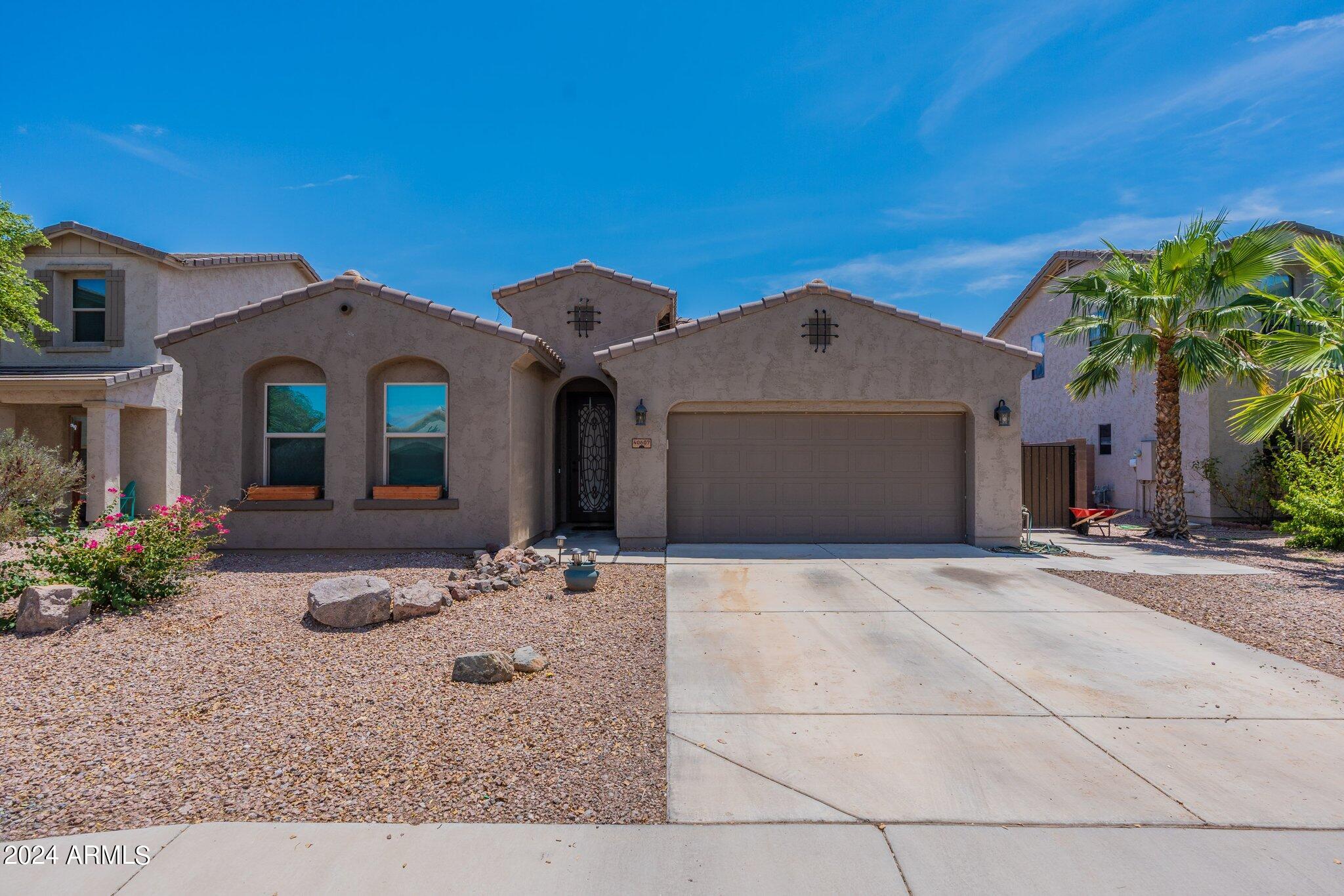 Stucco home with a two-car garage, gravel landscaping, and palm trees.