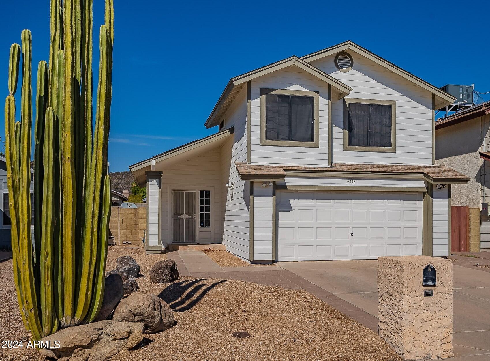 Two-story home with a two-car garage, fronted by a tall saguaro cactus and desert landscaping.
