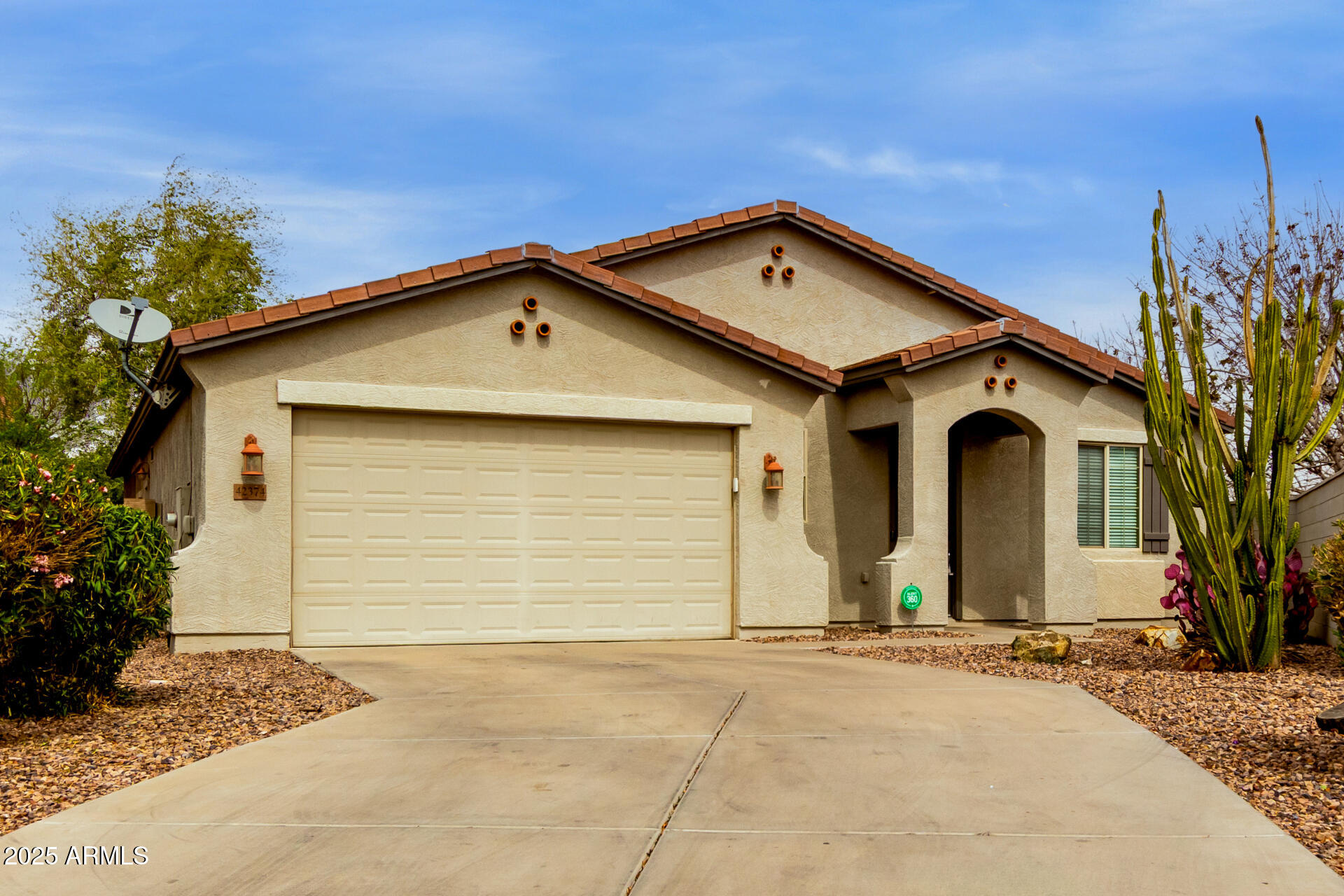 Stucco home with a red tile roof, two-car garage, and tall cacti in the desert landscaping.