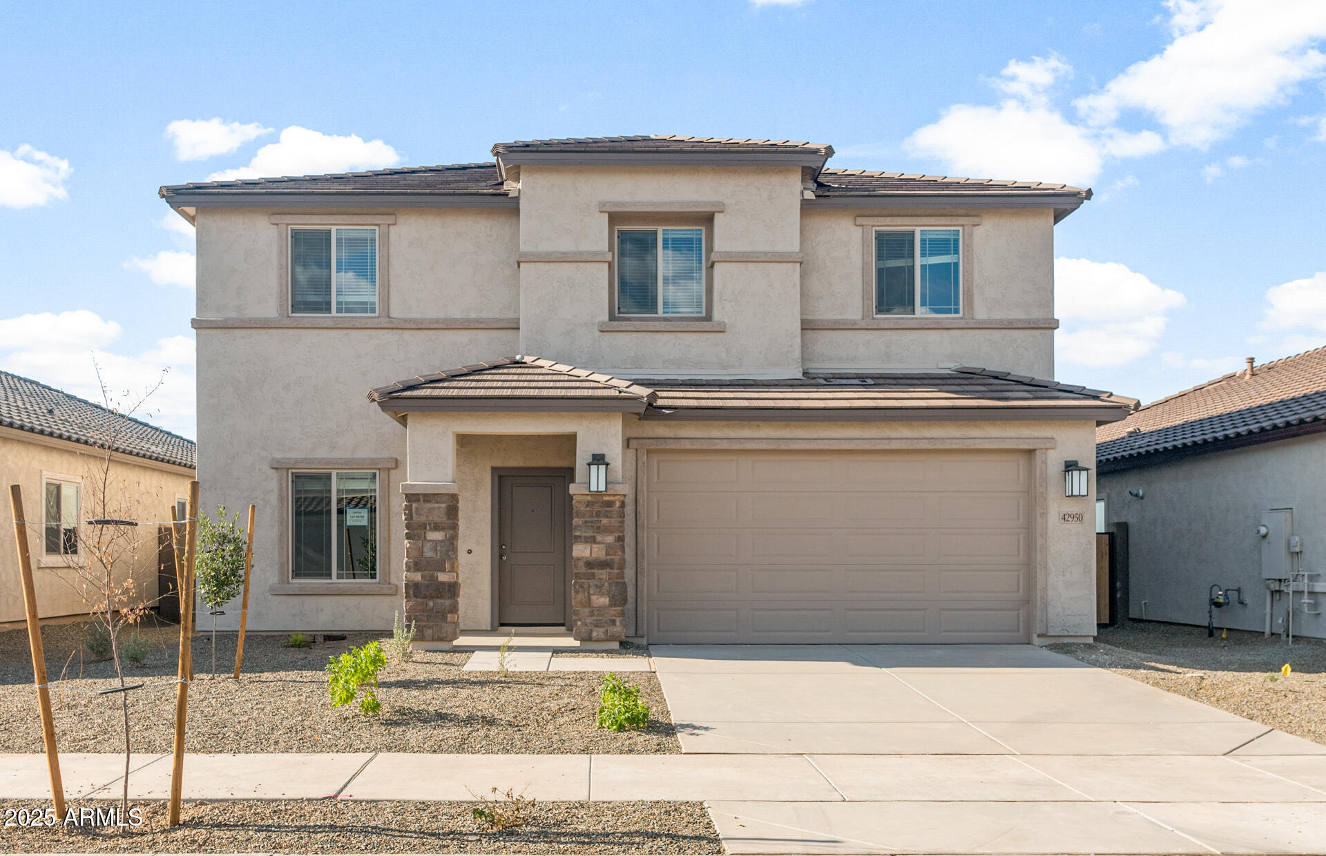 Two-story stucco home with stone entry accents, an attached garage, and a gravel front yard.