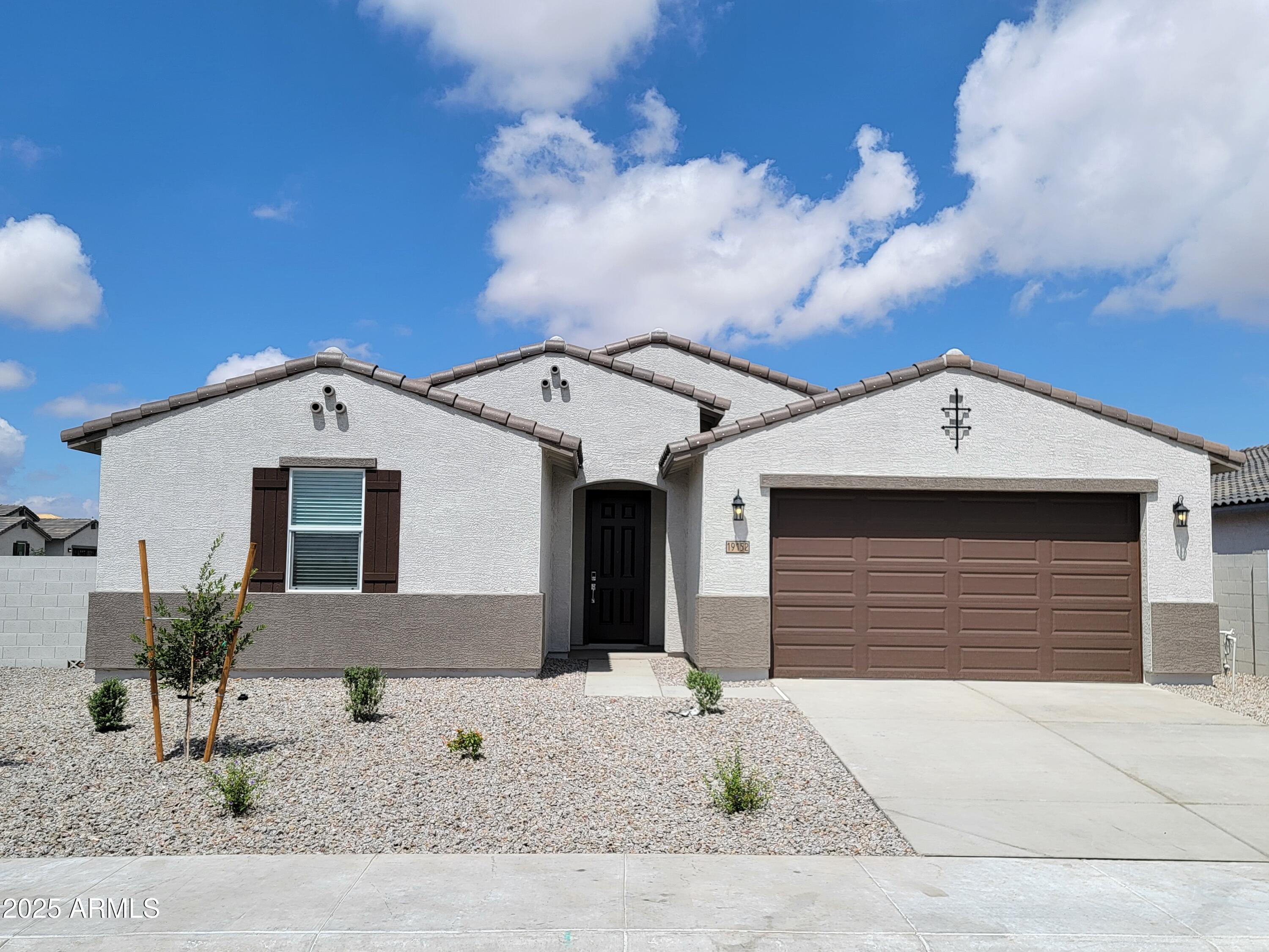 Single-story white stucco home with brown trim, a two-car garage, and gravel landscaping.