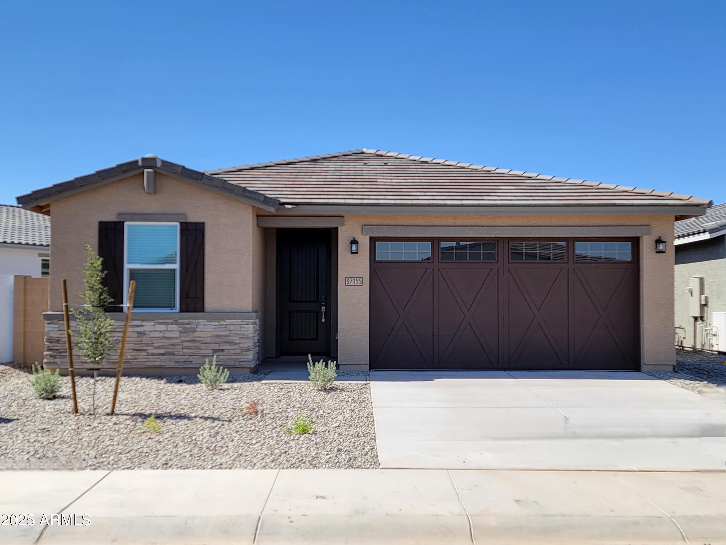 Home exterior with a dark double garage door, stone accents, tiled roof, and desert landscaping.