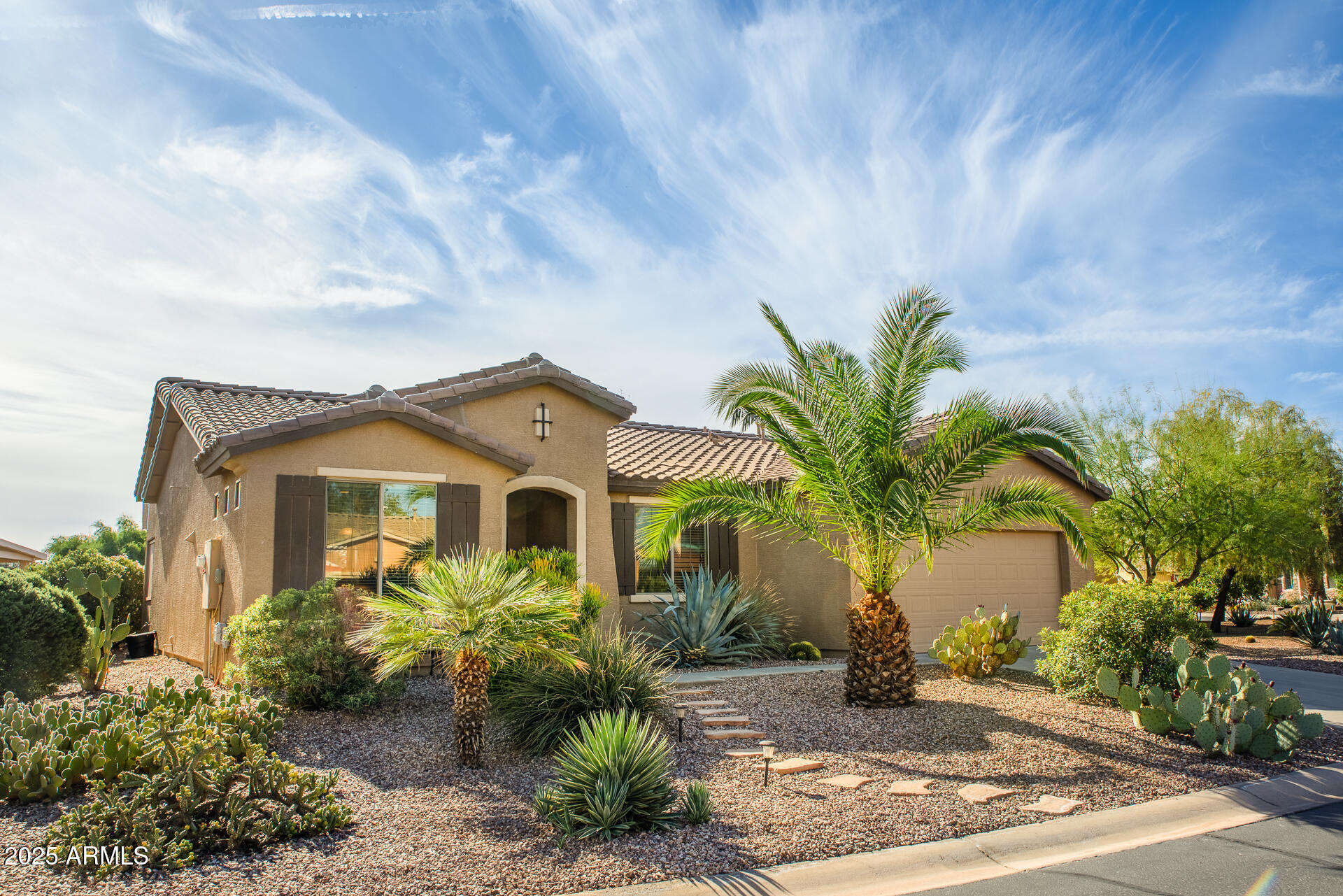 Tan stucco home with an attached garage, palm trees, and desert landscaping.