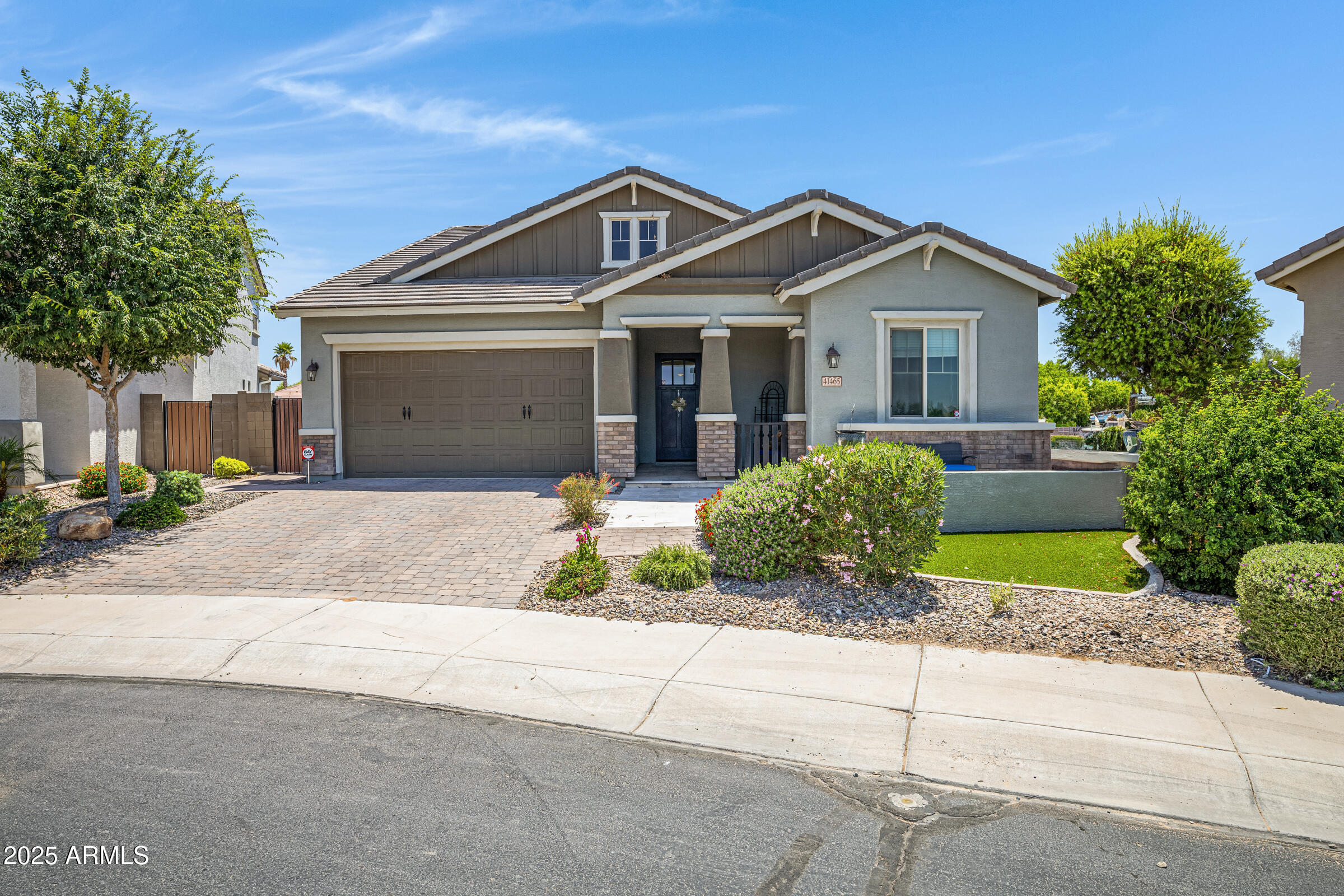 Gray stucco home with a two-car garage, paver driveway, covered entry, and landscaped front yard.
