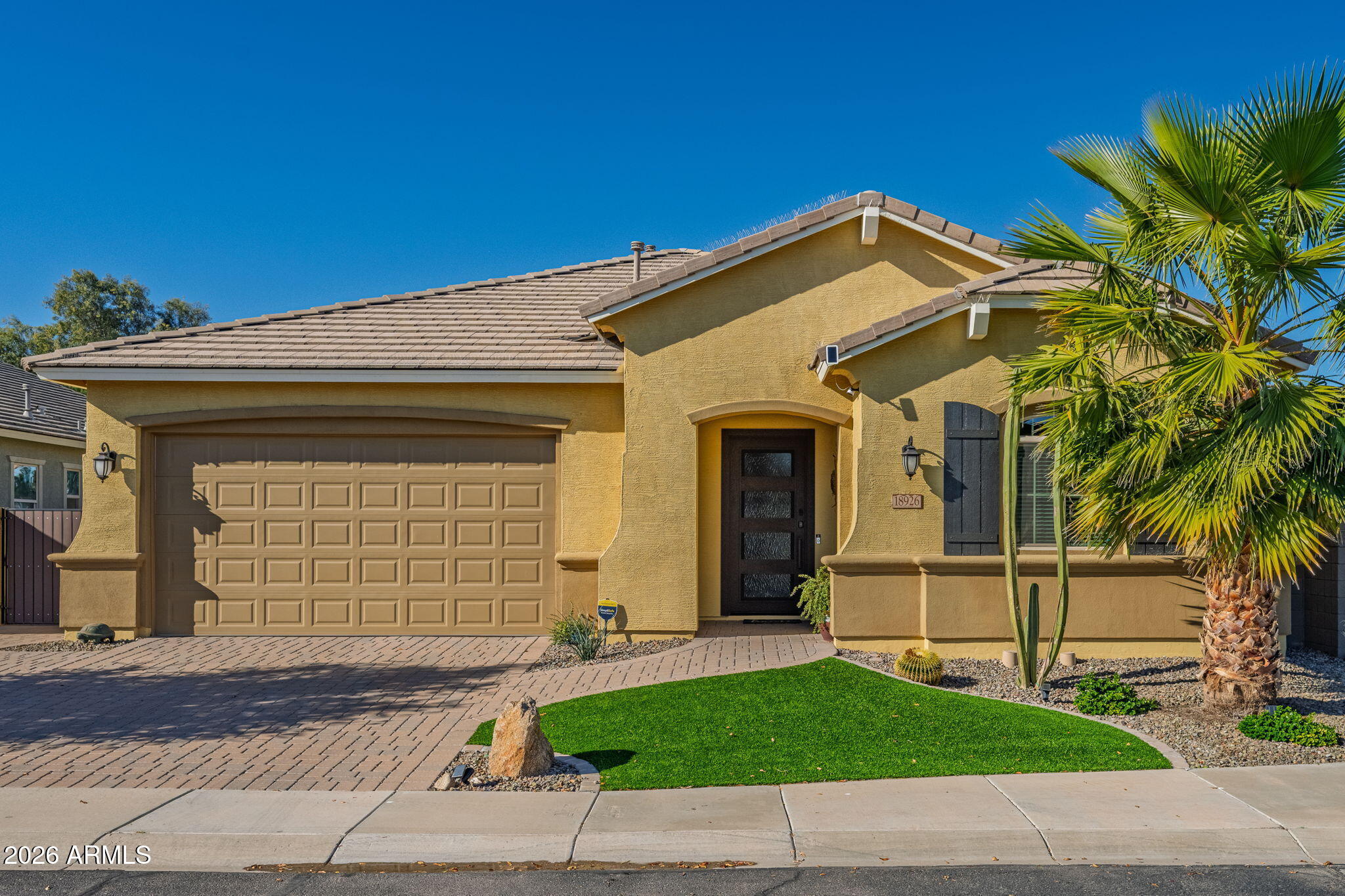 Tan stucco home with a two-car garage, palm trees, and a small green lawn.