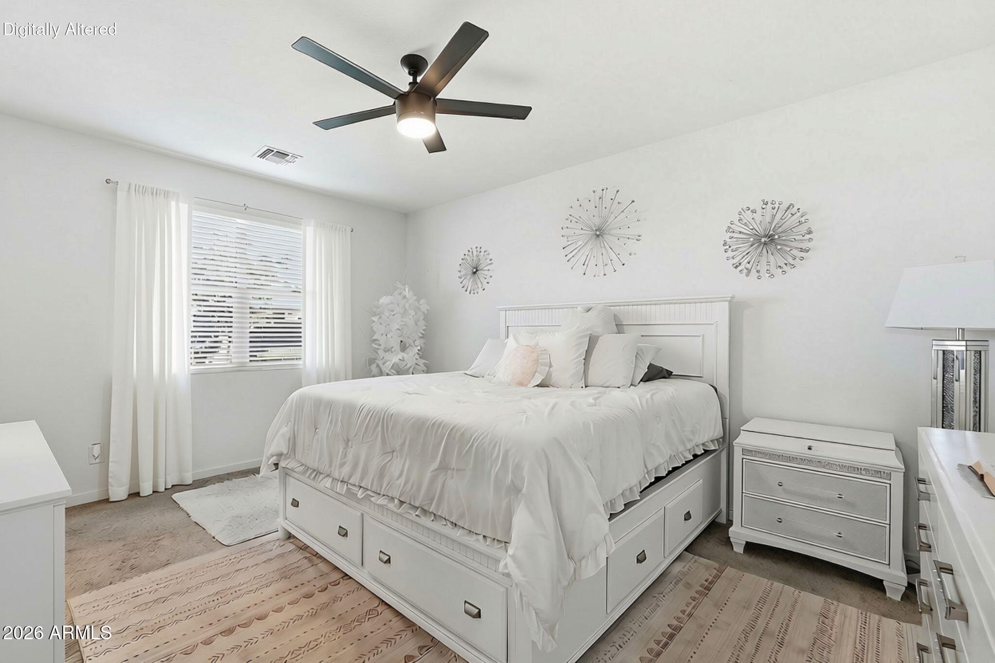 Bright white bedroom with a storage bed, matching furniture, patterned rugs, and a dark ceiling fan.