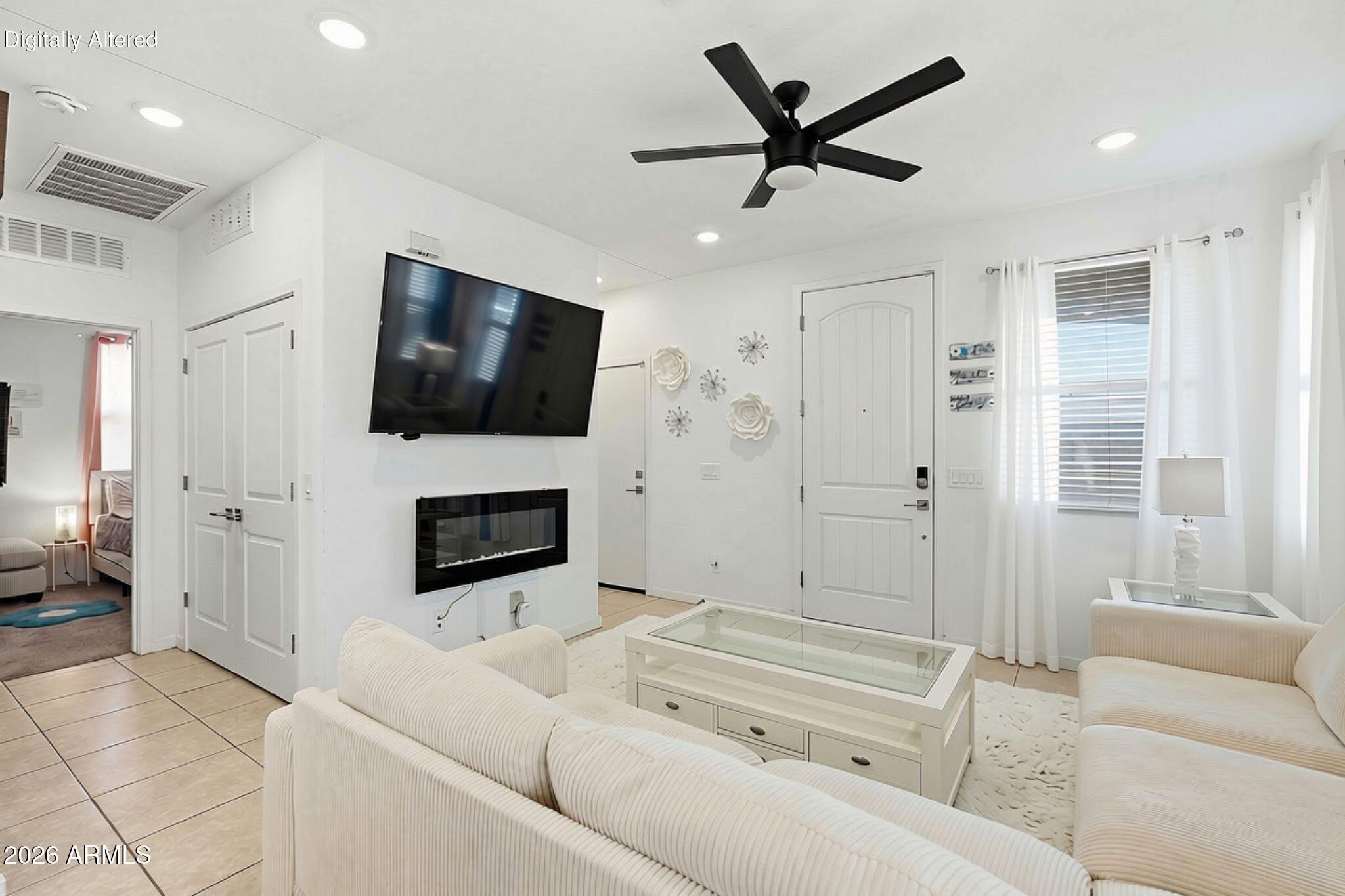 White living room with a wall-mounted TV above an electric fireplace and a black ceiling fan.