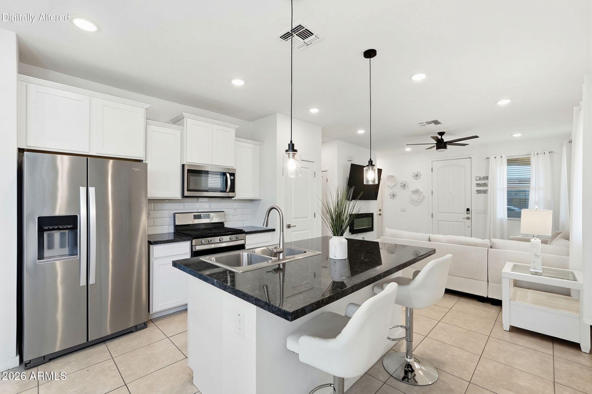 Open-plan kitchen with white cabinets, stainless steel appliances, and a black island adjoining a furnished living area.